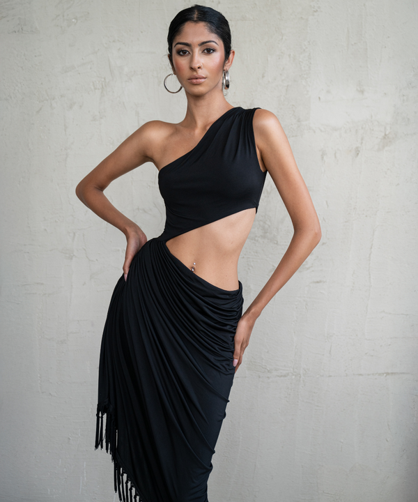 Woman wearing a black one-shoulder dress with fringe details against a gray background