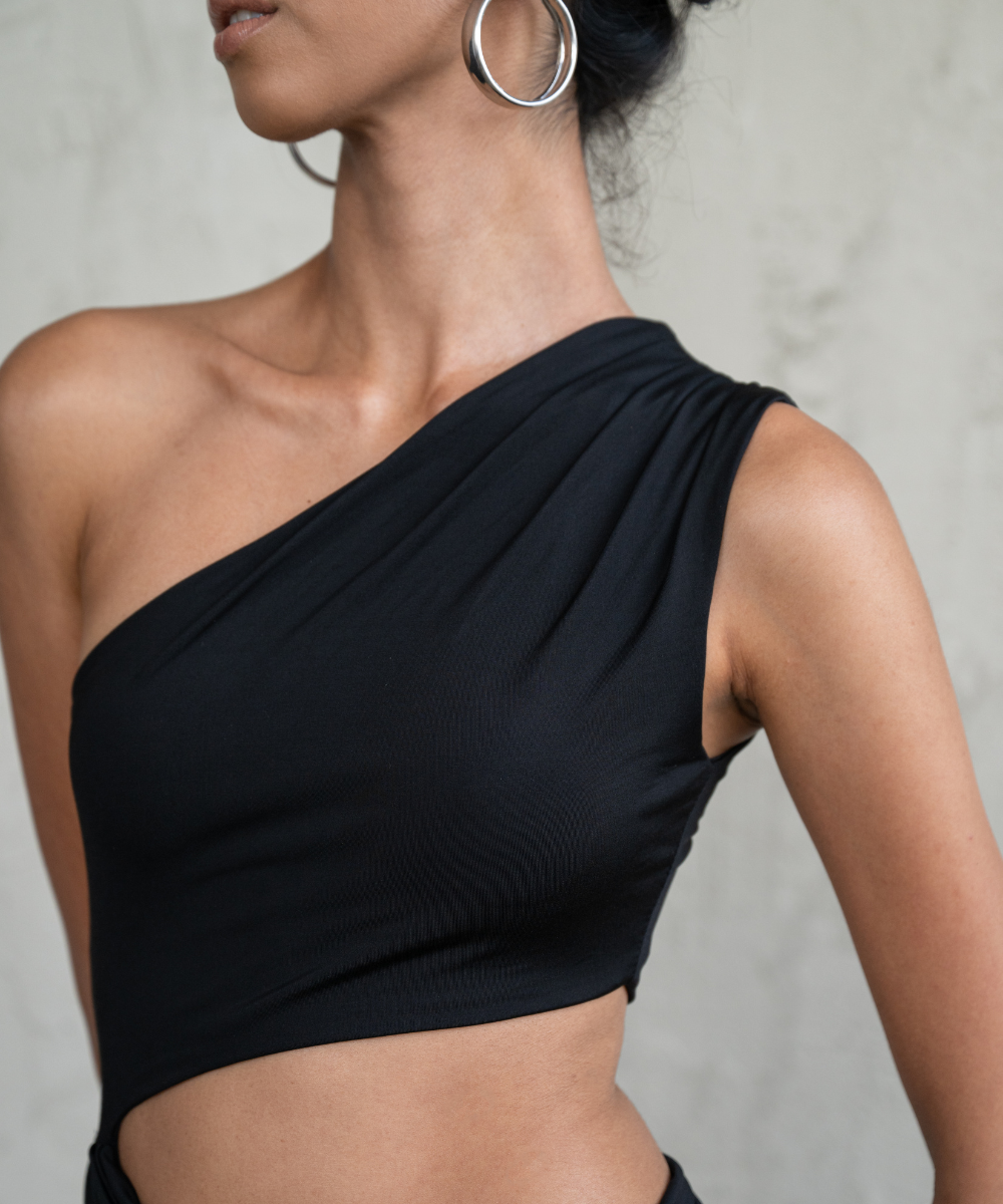 Black one-shoulder top worn by a model against a neutral background