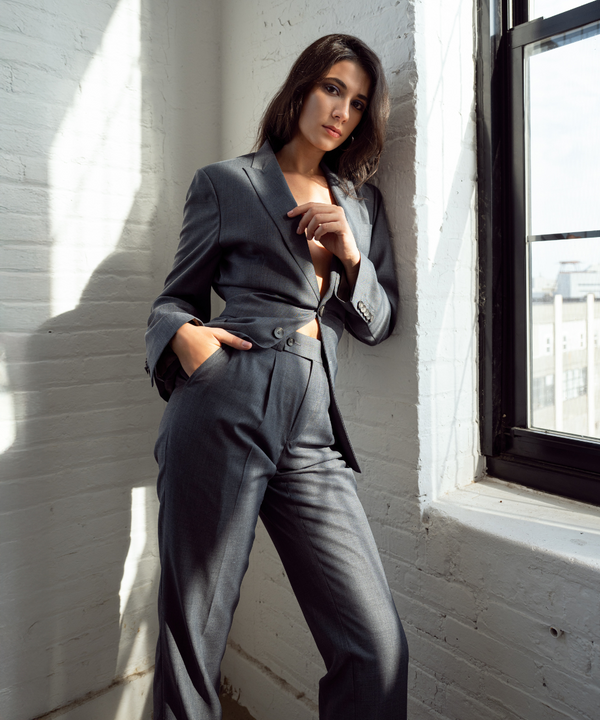 Woman in a gray suit standing by a window with white brick walls.