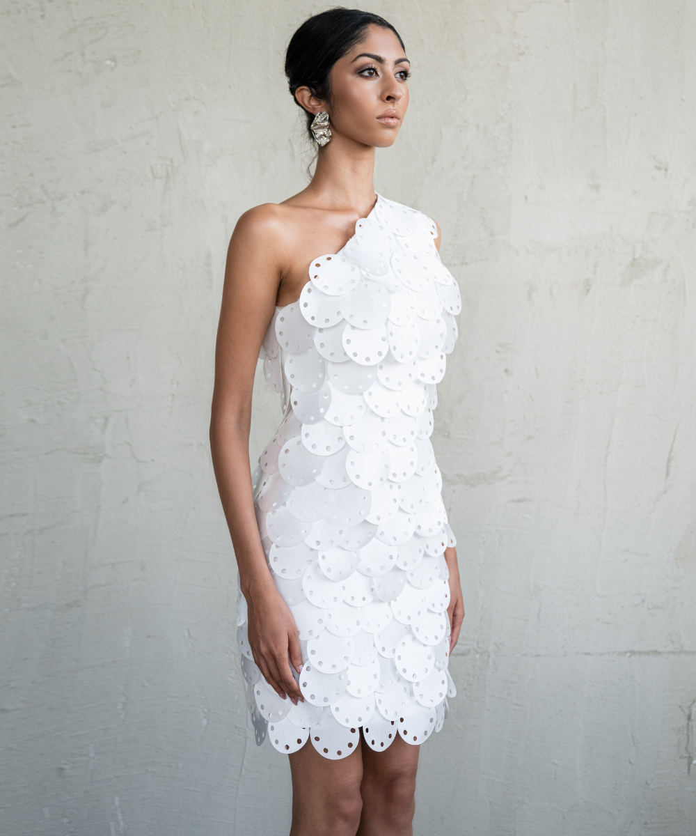 Woman wearing a white lace one-shoulder dress against a plain background